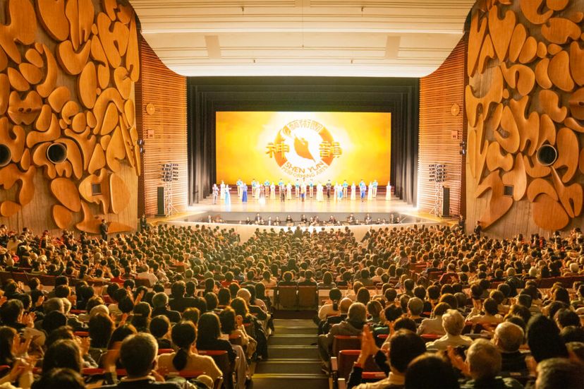 木の彫刻の壁に囲まれた満員の客席。神韻のロゴが映る舞台に出演者が並び、観客が拍手している